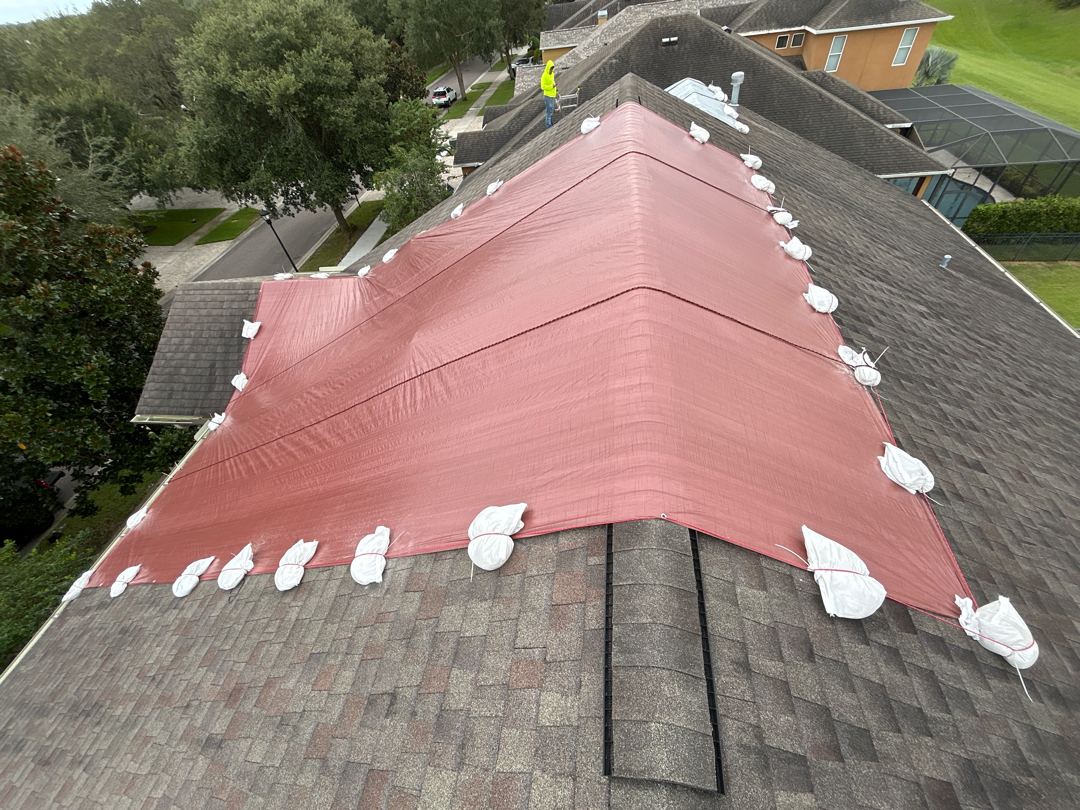 Aerial view of full-slope red emergency tarp install with sandbag securement on Florida shingle roof