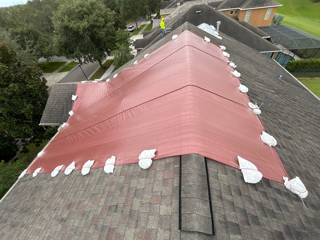 Aerial view of full-slope red emergency tarp install with sandbag securement on Florida shingle roof