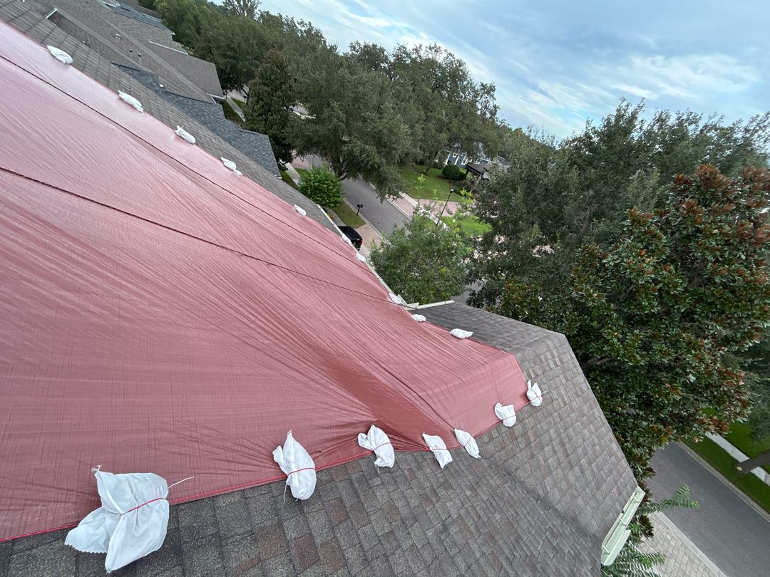 Close aerial of red tarp draped over hip roof with sandbag perimeter