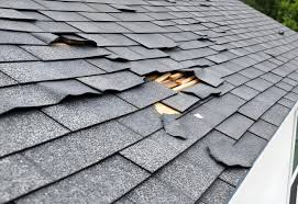 Torn and missing shingles with exposed wood decking near roof edge