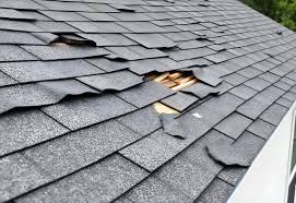 Torn and missing shingles with exposed wood decking near roof edge