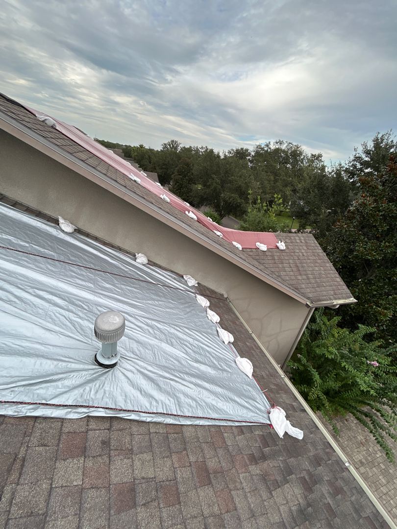 Wide angle of white tarp install with red and white tarp sections meeting at hip ridge